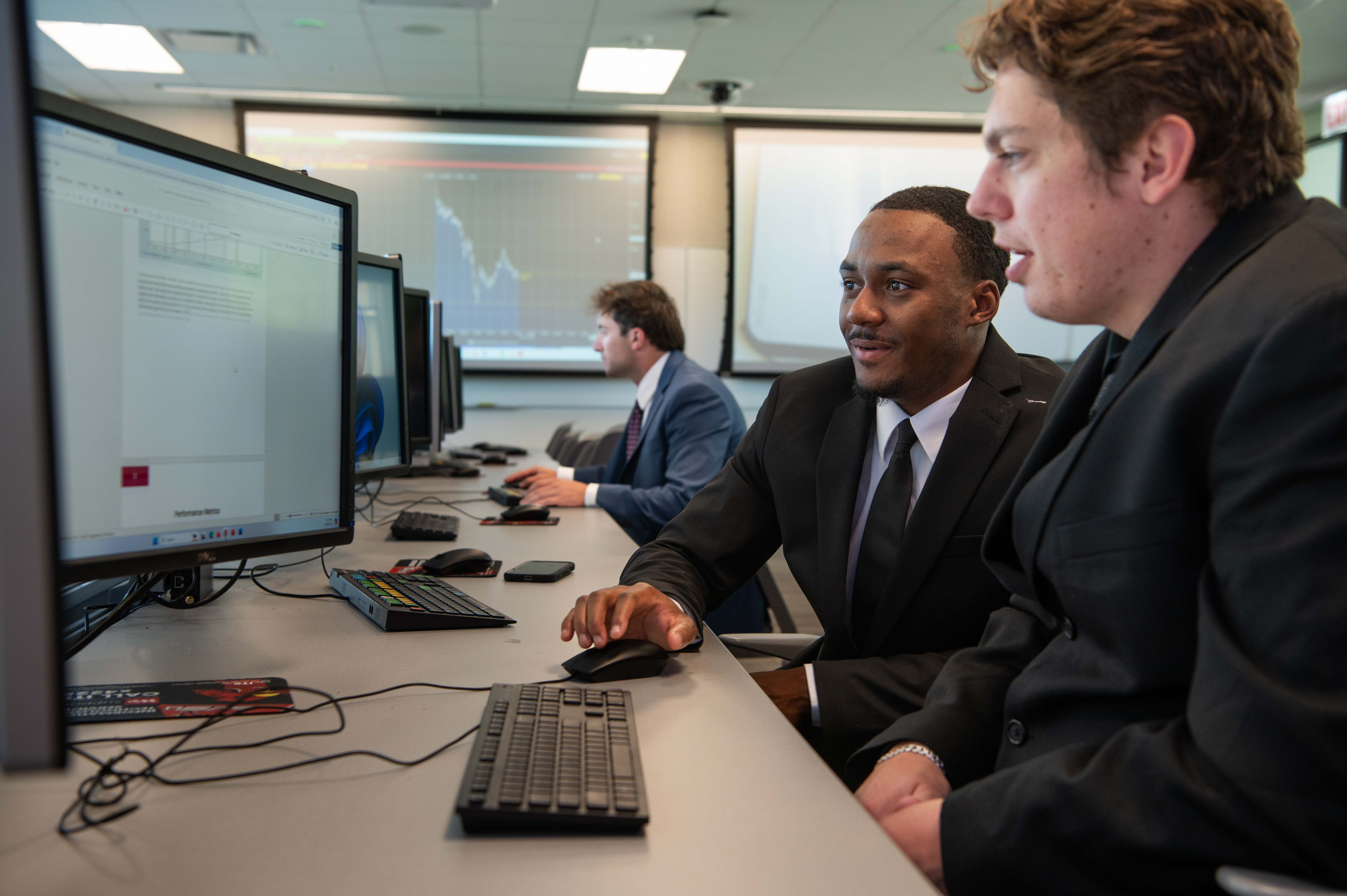 two students looking at computer screen; another student in background